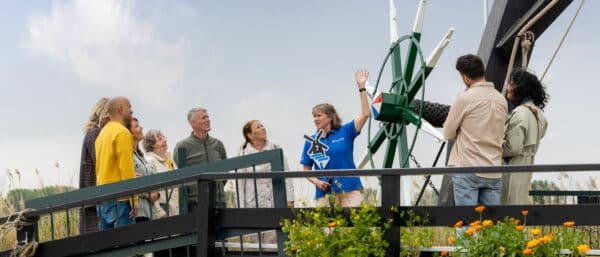 Gids in Kinderdijk-kleding heeft uitleg aan een groep bezoekers bij Museummolen Nederwaard in Kinderdijk