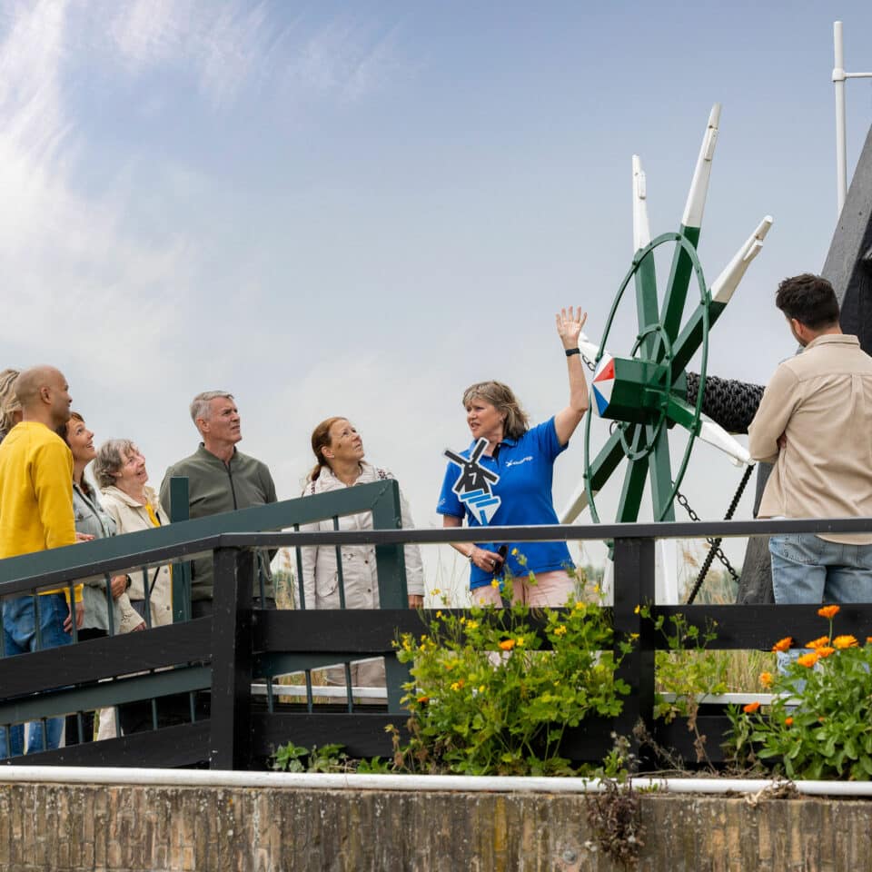 Gids in Kinderdijk-kleding heeft uitleg aan een groep bezoekers bij Museummolen Nederwaard in Kinderdijk