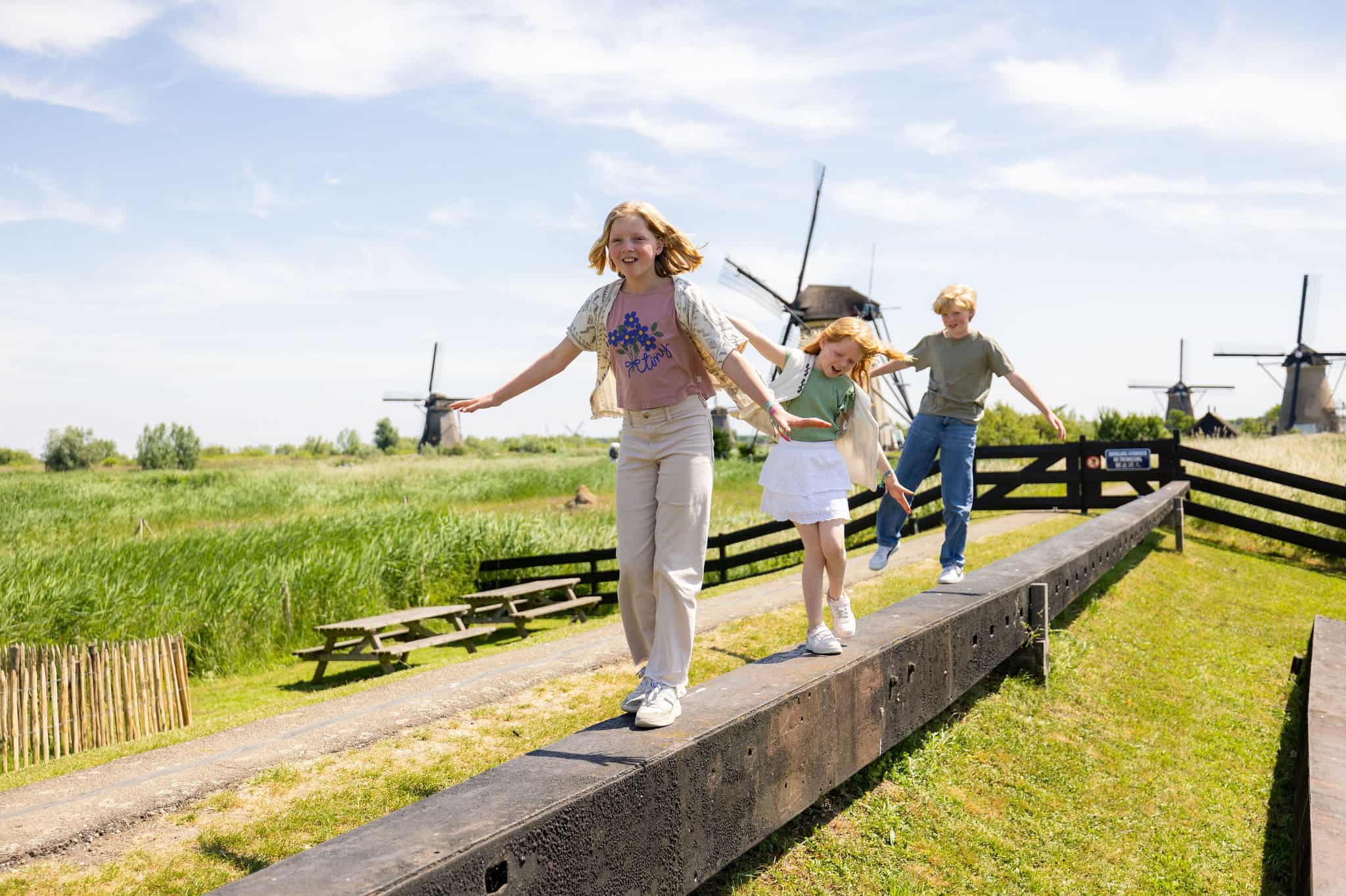 Kids balancing on a beam with windmills behind them