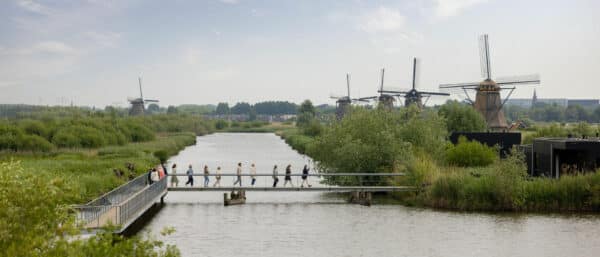 Mensen betreden UNESCO Werelderfgoed Kinderdijk via de brug van de groepsentree. Op de achtergrond zijn de molens al te zien