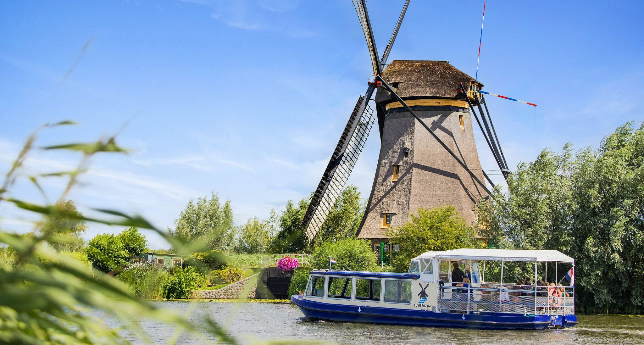The Hopper sightseeing boat sails past a windmill in Kinderdijk with visitors on board.