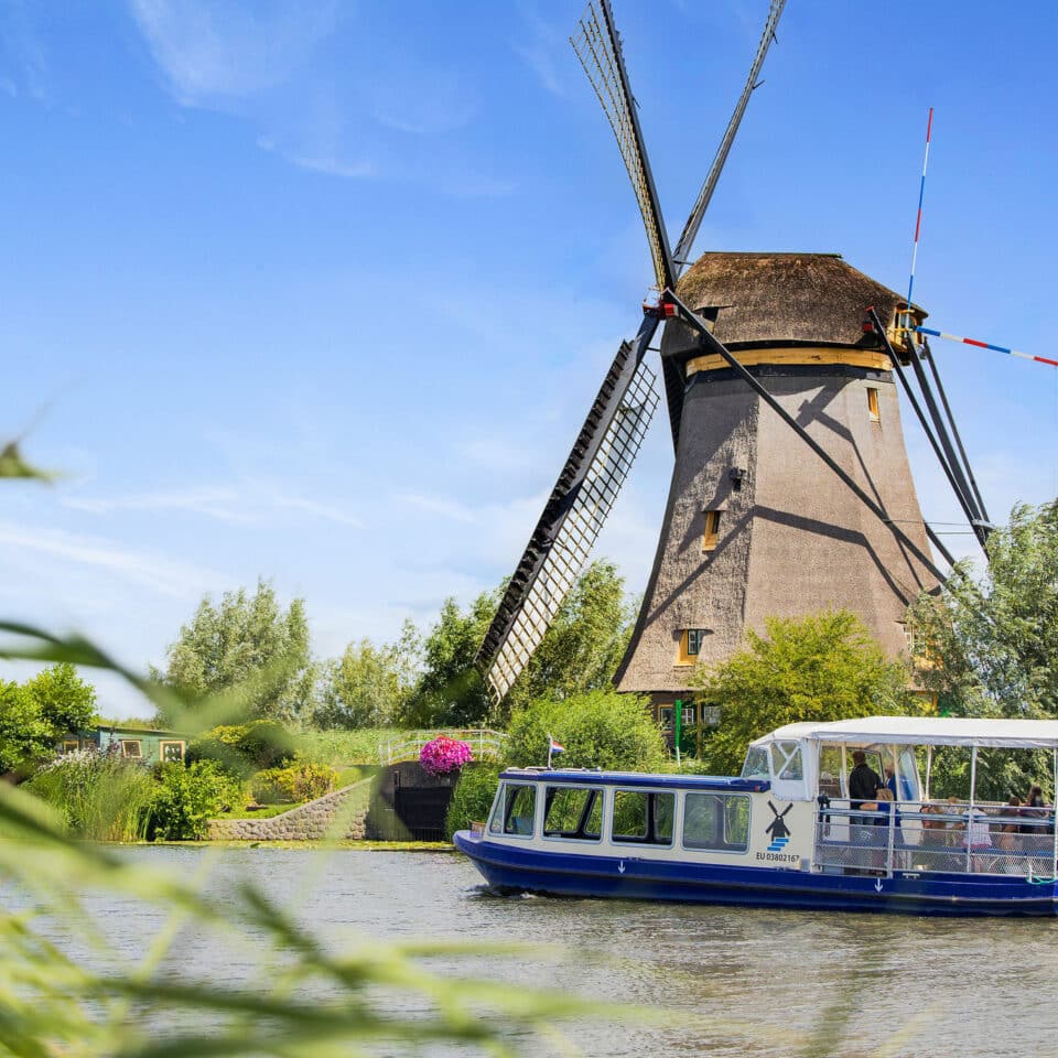 The Hopper sightseeing boat sails past a windmill in Kinderdijk with visitors on board.