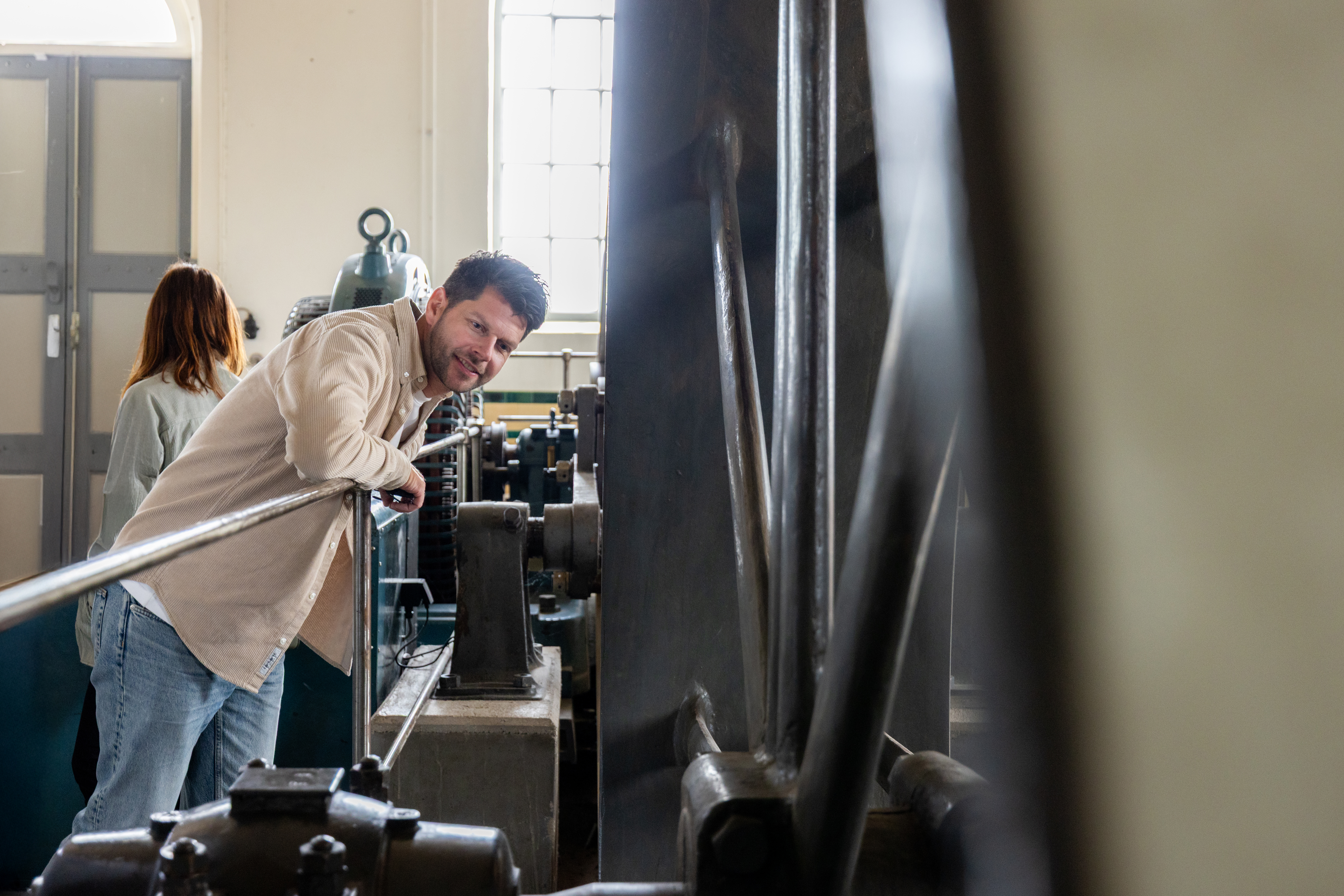 Een man half hangend over de reling kijkende naar het vliegwiel in het Wisboomgemaal in Kinderdijk