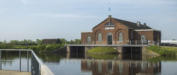 Vanaf een brug kijk je naar het Wisboomgemaal in Kinderdijk met een mooie reflectie op het water