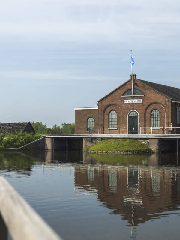 Vanaf een brug kijk je naar het Wisboomgemaal in Kinderdijk met een mooie reflectie op het water