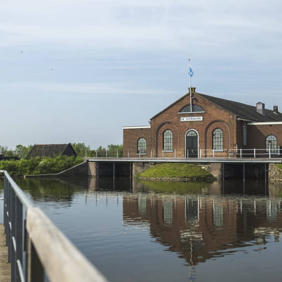 From a bridge, you look toward the Wisboom Pumping Station in Kinderdijk, with a beautiful reflection on the water.
