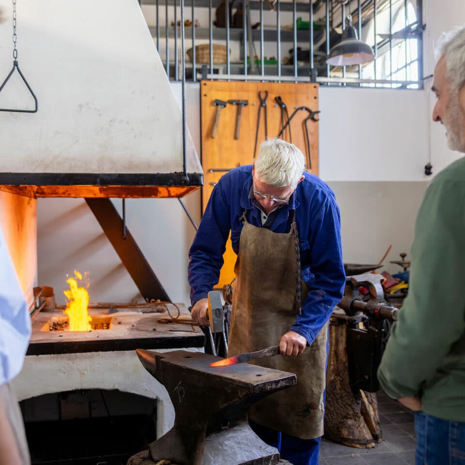 Bezoekers kijken toe hoe een vrijwillig smid aan het werk is in de smidse van het Wisboomgemaal in Kinderdijk