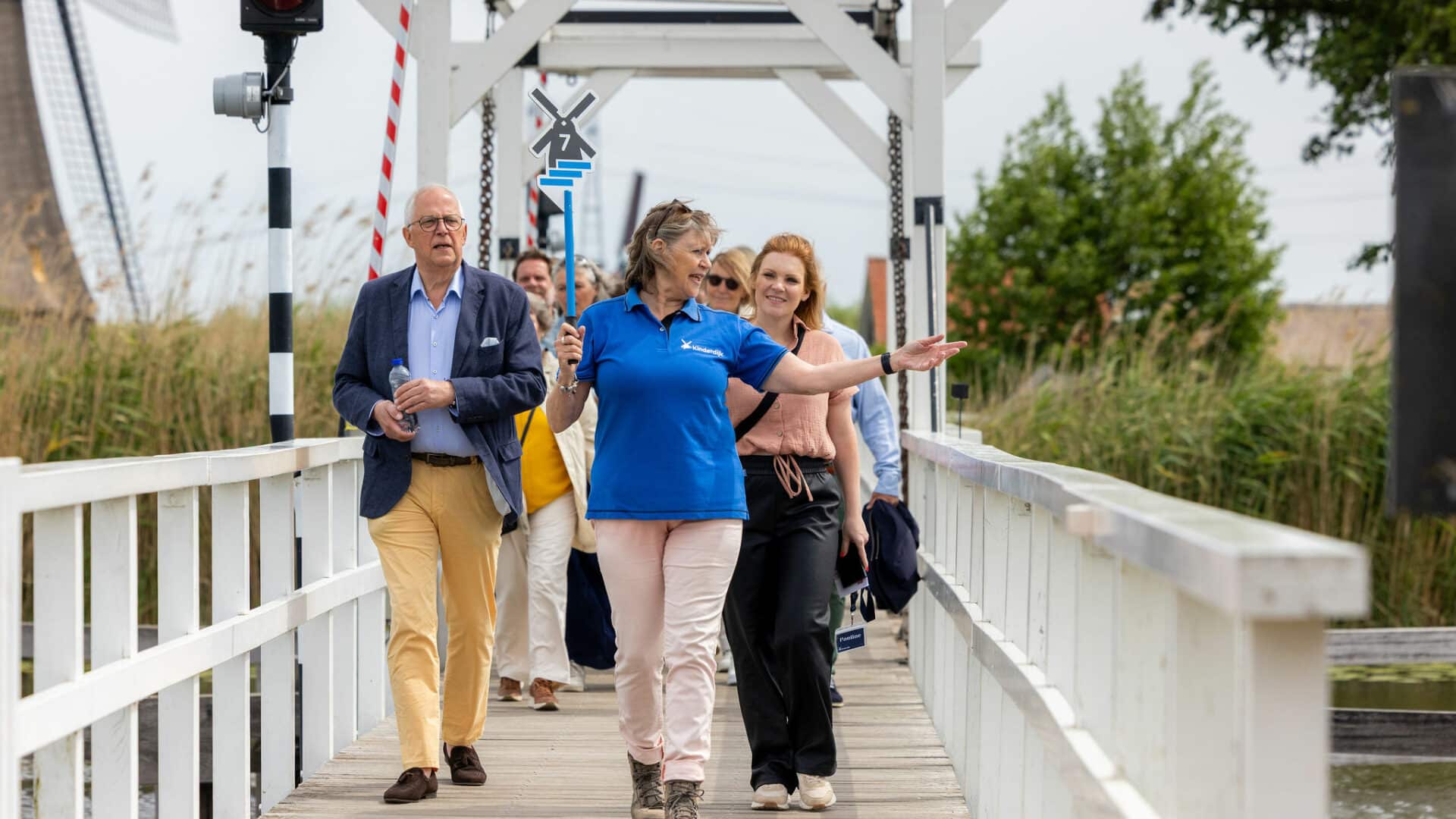 Gids loopt over de brug met een groep bezoekers naar de molen in Kinderdijk.