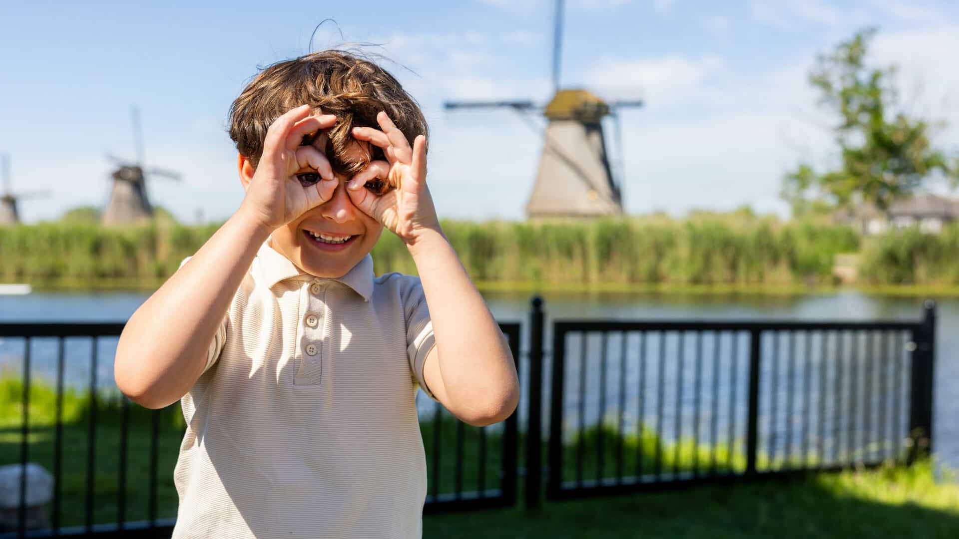 Kind maakt een grappig gezicht in Kinderdijk met op de achtergrond een molen.