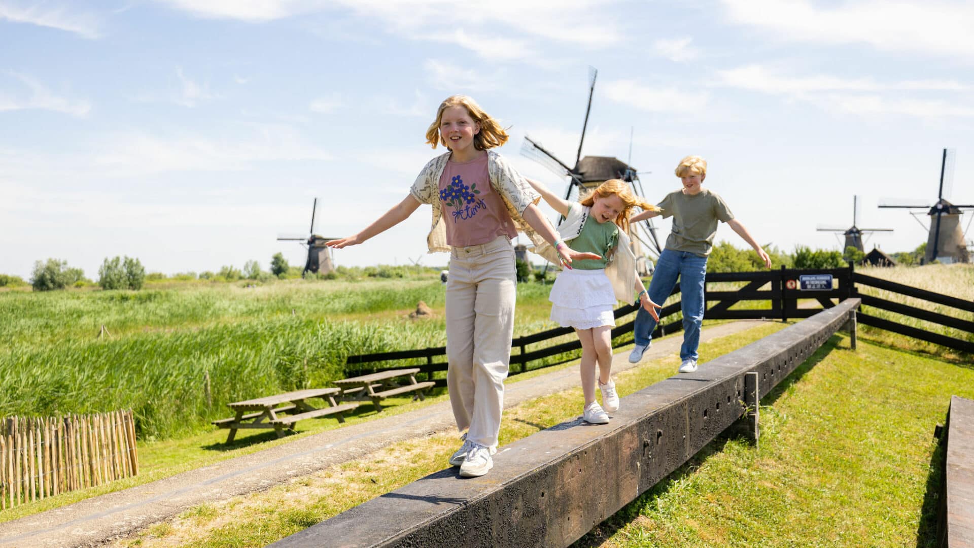Drie kinderen spelen op de molenroede op het erf van Museummolen Nederwaard met op de achtergrond de molens van Kinderdijk