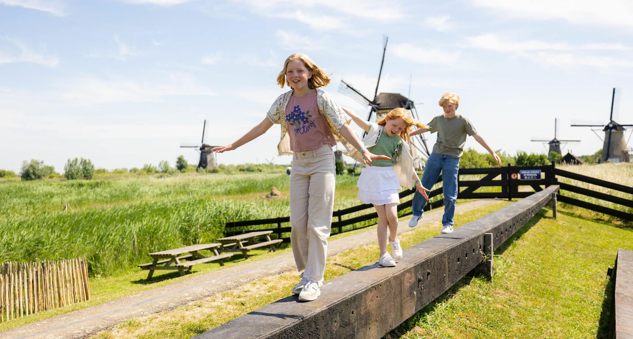 Drie kinderen spelen op de molenroede op het erf van Museummolen Nederwaard met op de achtergrond de molens van Kinderdijk