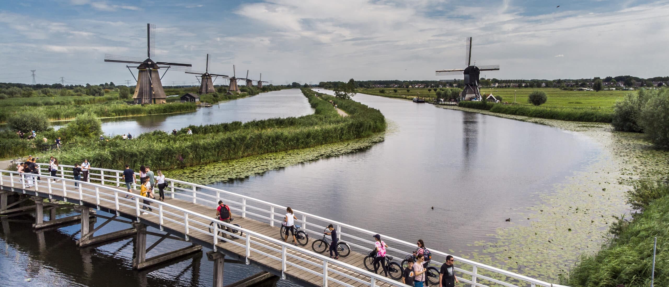 Luchtfoto in Kinderdijk van de molens van de Overwaard en de Blokweer. Op de voorgrond is de brug te zien met toeristen.