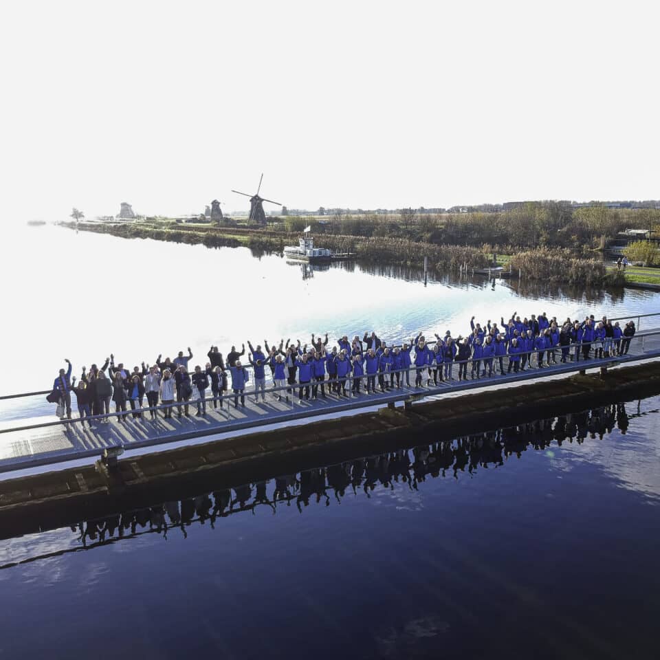 De medewerkers en vrijwilligers van Kinderdijk op de brug met op de achtergrond in de verte de molens.