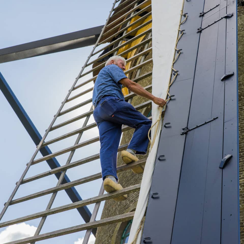 Een molenaar op klompen in de wieken van de museummolen in Kinderdijk