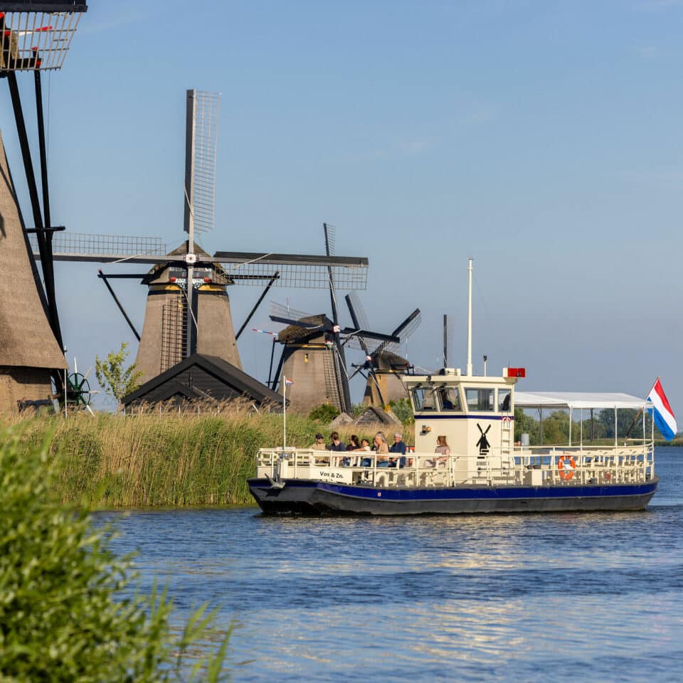 De rondvaartboot Cruiser vaart met bezoekers in Kinderdijk met op de achtergrond de molens van de Overwaard.