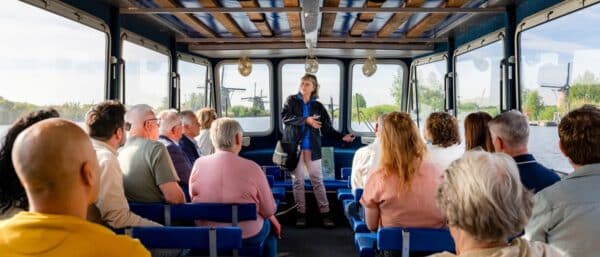 Een groep aan boord van de rondvaartboot in Kinderdijk krijgt uitleg van een gids terwijl zij langs de molens varen.