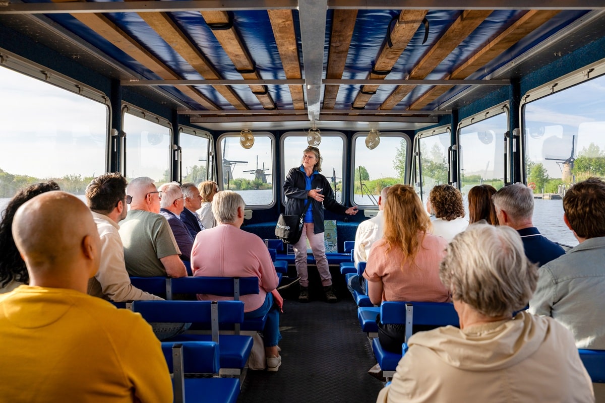 Een groep aan boord van de rondvaartboot in Kinderdijk krijgt uitleg van een gids terwijl zij langs de molens varen.