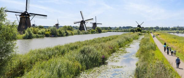 Mensen wandelend over de Middelkade in Kinderdijk met uitzicht op de molens op een mooie zomerse dag