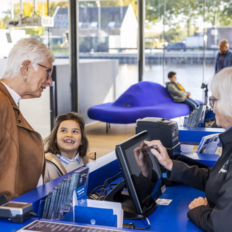 Een vrijwilliger in Kinderdijk helpt bezoekers bij het aanschaffen van de tickets in het Bezoekerscentrum.