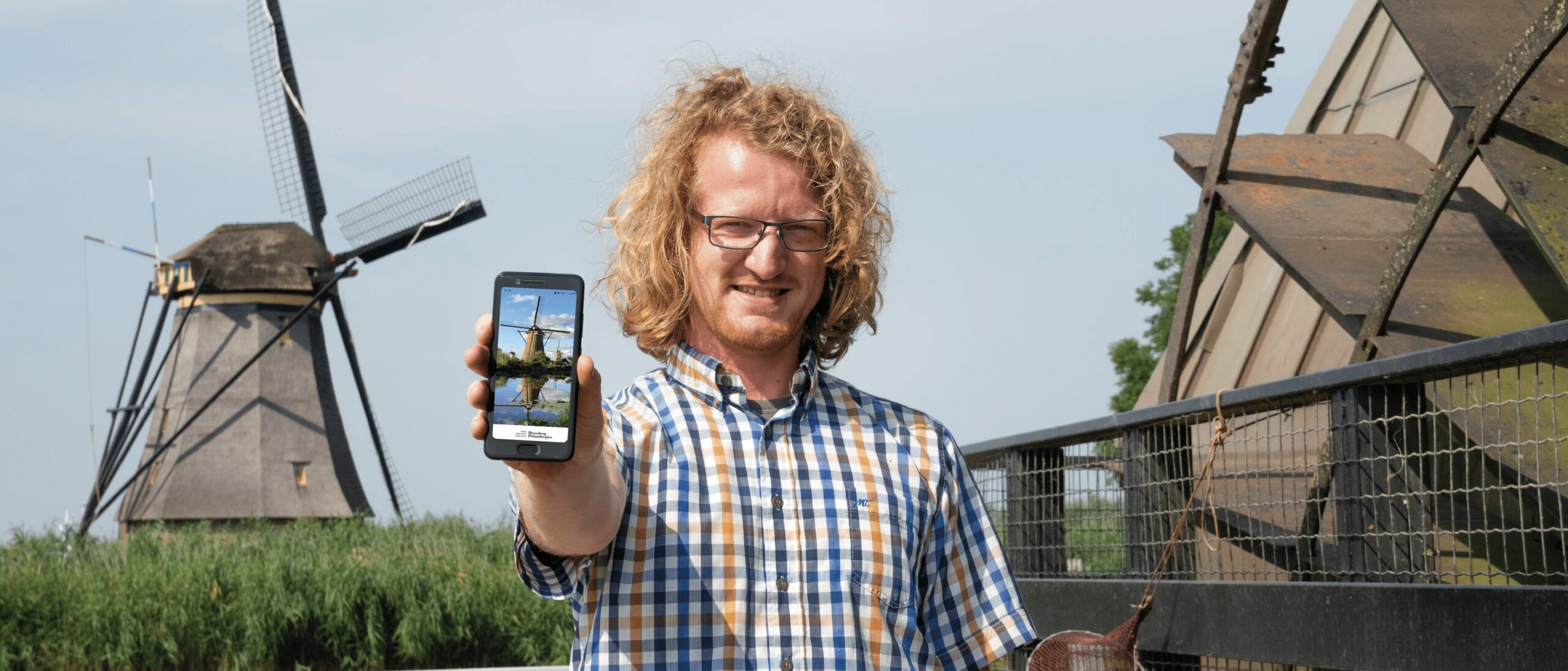 Molenaar houdt telefoon vast waarop de audiotour van Kinderdijk te zien is
