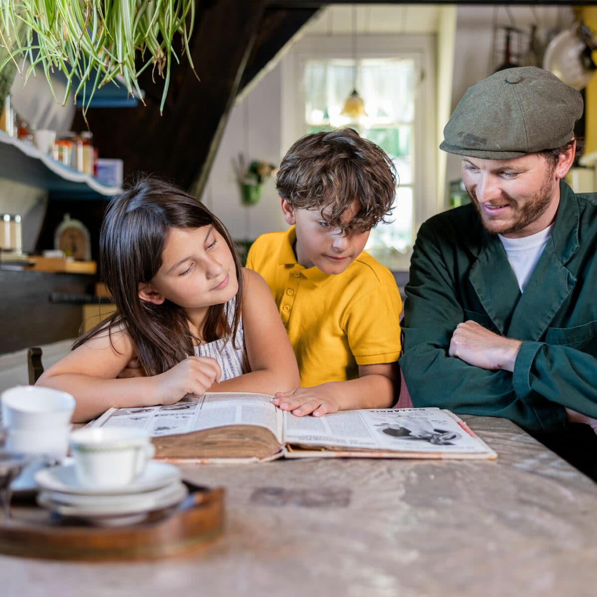 Molenaar in de woonkamer van Museummolen Blokweer neemt samen met twee kinderen een boek door