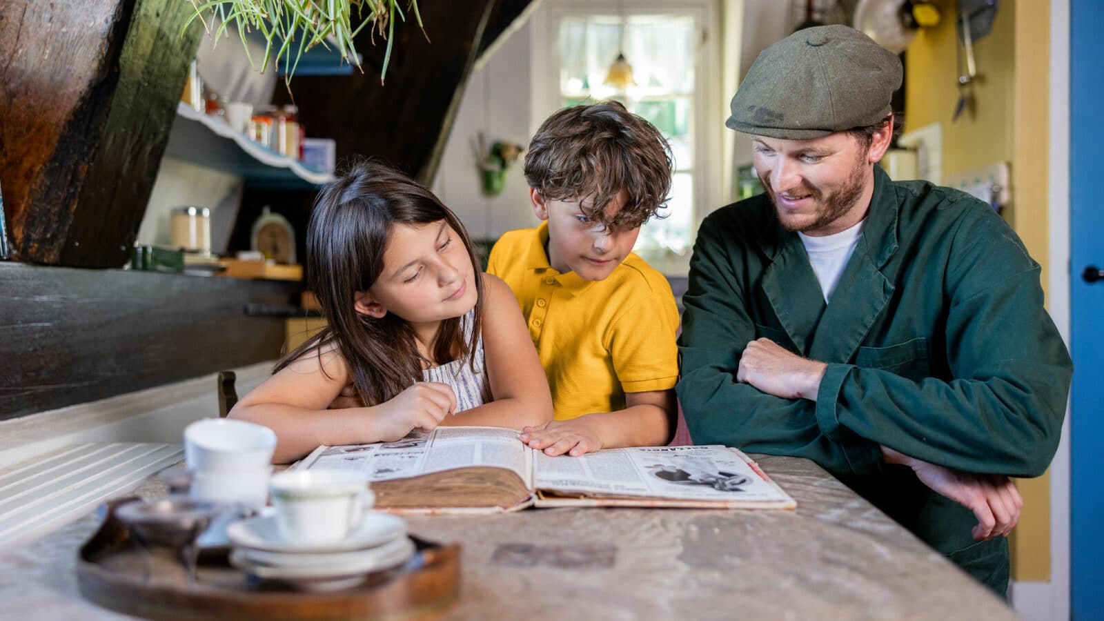 Molenaar in de woonkamer van Museummolen Blokweer neemt samen met twee kinderen een boek door