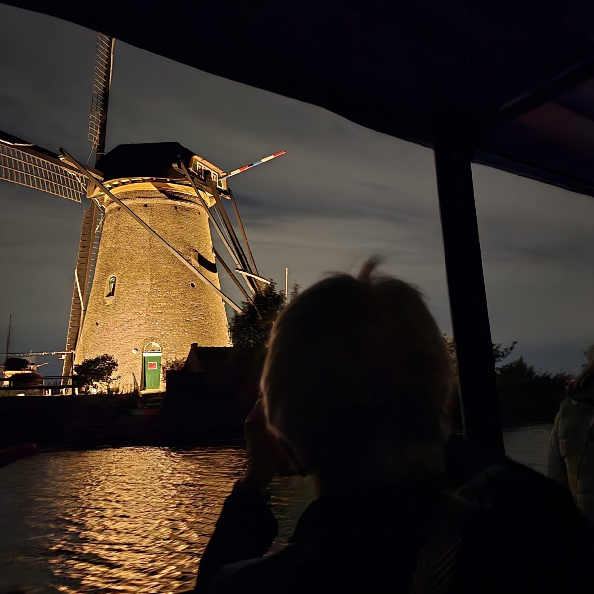 An illuminated windmill seen from a tour boat during Illumination Week in Kinderdijk.